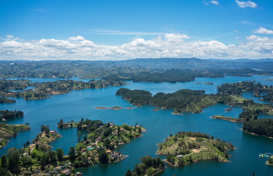 Aerial view of Guatapé’s emerald reservoir dotted with lush islets under a bright sky.