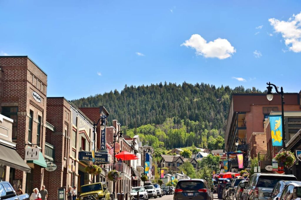 Brick-front shops lining a sunlit main street beneath forested hills in Evergreen, Colorado