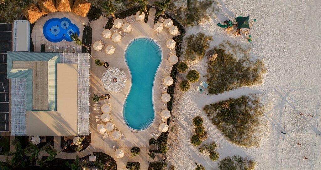Curving pool flanked by sandy shore and umbrellas at Sirata Beach Resort