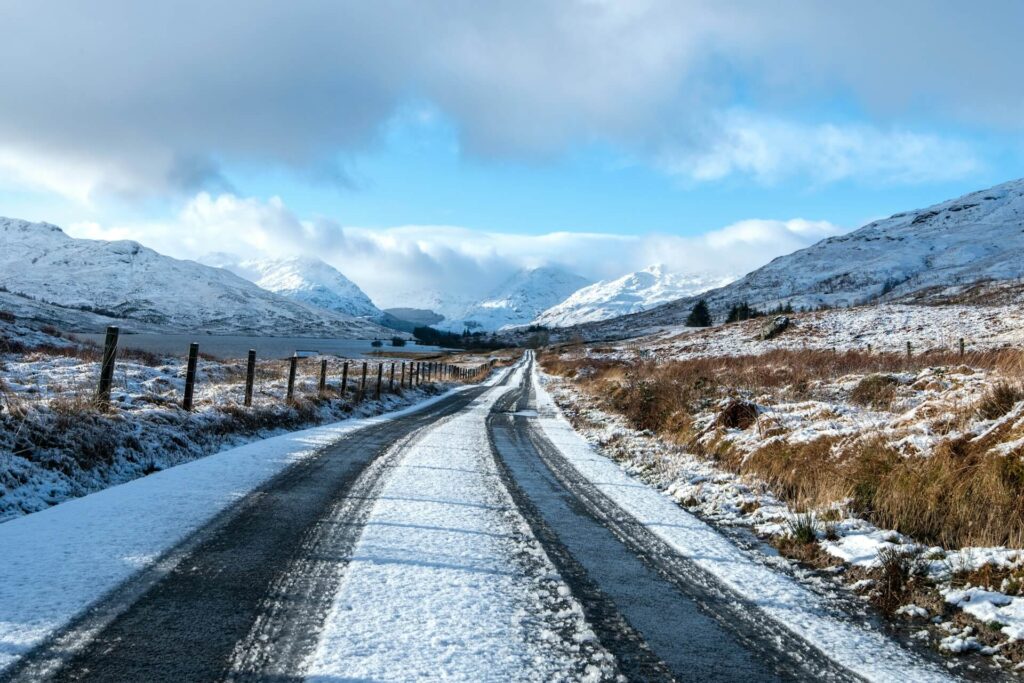 Snow-dusted road framed by towering peaks on a crisp winter morning in the Scottish Highlands
