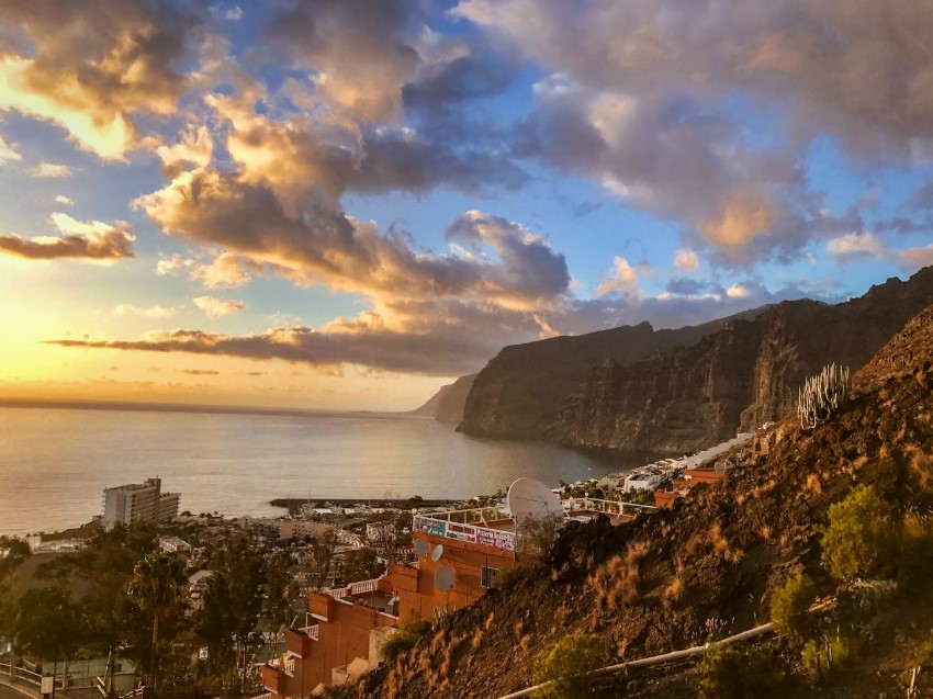 Sunset clouds glowing over rugged cliffs and seaside town in the Canary Islands.