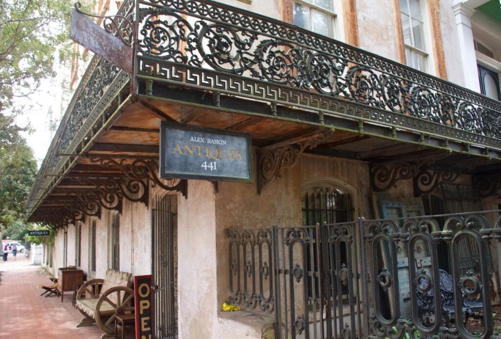 Time-worn Alex Raskin Antiques storefront crowned by intricate wrought-iron balcony