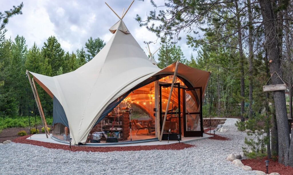 Canvas-topped glamping tent illuminated among trees at Under Canvas Glacier