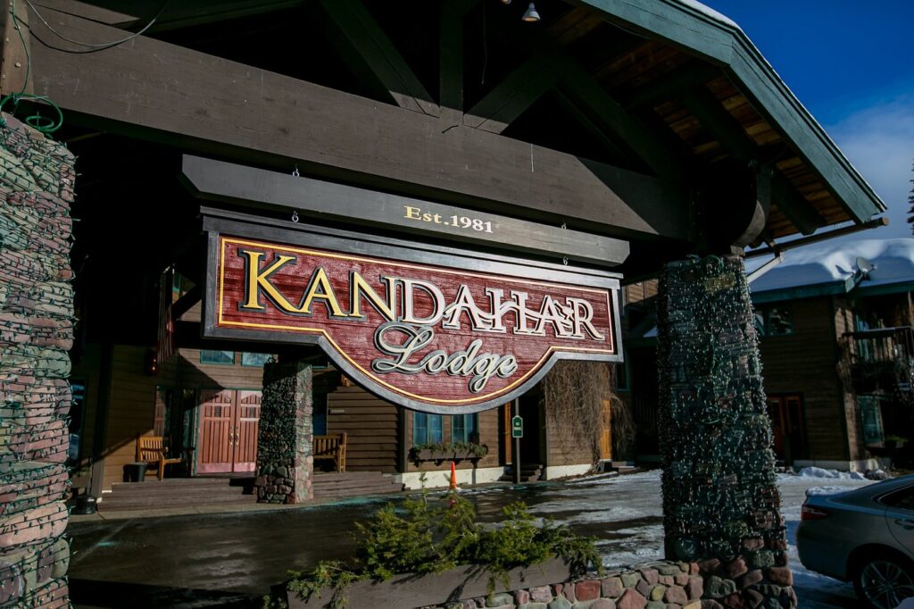 Hand-carved entrance sign beneath log rafters at Kandahar Lodge, Whitefish Mountain Resort